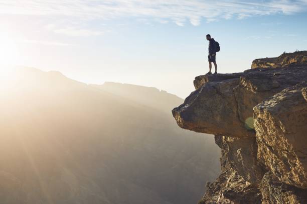 Personalised Travel 36 Young tourist with backpack standing on the edge of cliff at sunrise. Jebel Akhdar, Grand Canyon of Oman.