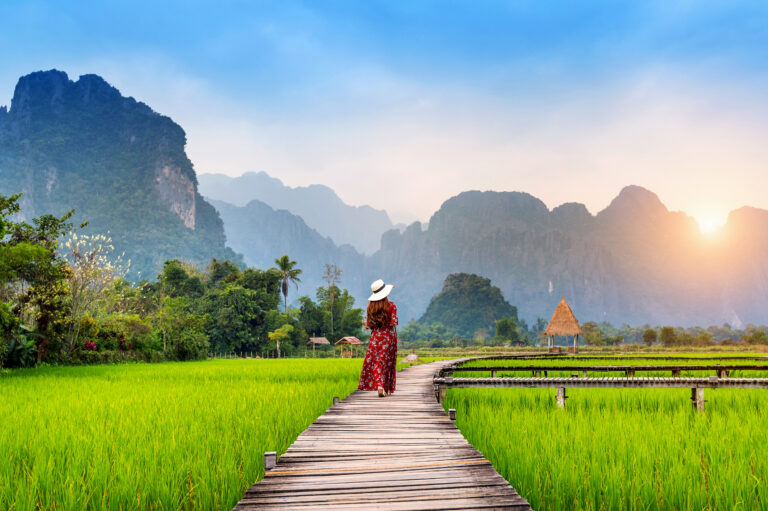 Personalised Travel 32 Young woman walking on wooden path with green rice field in Vang Vieng, Laos.